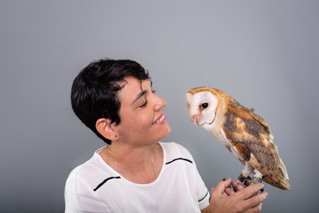 A woman lovingly looking at her owl. Wild animals. Against gray background.の写真素材