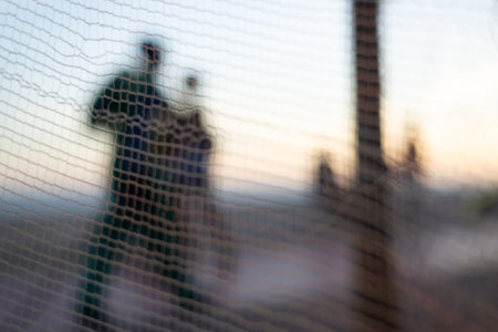 Silhouette of people, through a safety net, walking along the edge of a beach in the late afternoon. Abstract photography concept.の写真素材
