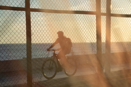 Silhouette of cyclists and people walking on the edge of a beach against sunset. Practice of...