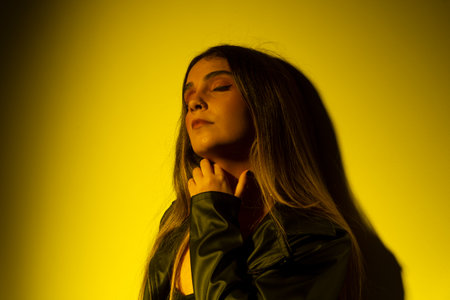 Portrait of beautiful young model with straight hair leaning on a yellow -illuminated wall. studio photoの写真素材