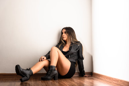Beautiful young model wearing black, casual clothes, sitting on the wooden floor found on a white wall. Studio portrait.の写真素材