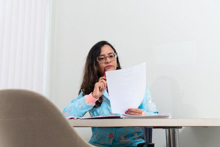 Portrait of a psychopedagogue in her office, wearing a colorful coat, sitting, making notes on paper. Helps with school performance. Take care of your mental health.の写真素材