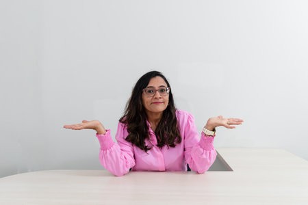 Portrait of a psychopedagogue, wearing pink clothes, in her office, sitting, making a sign with her hand. Helps with school performance. Take care of your mental health.の写真素材