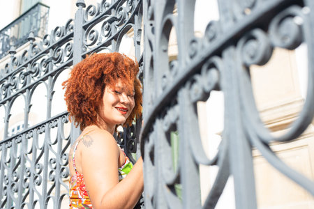 Portrait of a mature and beautiful redhead woman, wearing a colorful dress and her face leaning against an iron railing. Happy traveling person.の写真素材