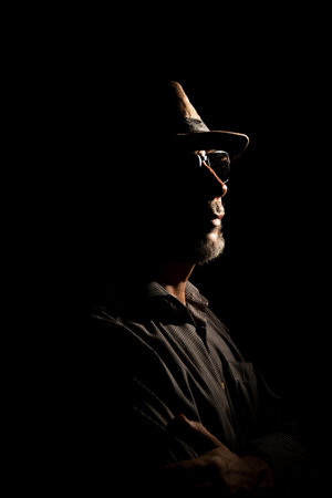 Discreet portrait of detective man with hat in darkness. Dark room art.