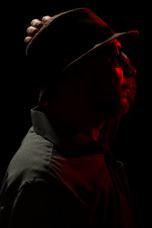 Discreet portrait of man wearing hat and sunglasses in darkness with red light on face. Dark room art.の写真素材