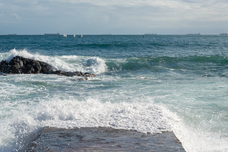 Waves from the rough sea crash heavily onto a beach pier. Wild nature. Seasons