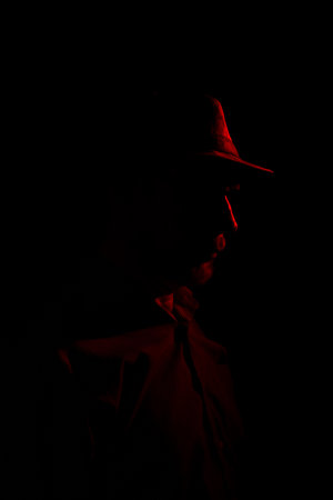 Man with hat on dark background, wearing sunglasses with red light on his face. Studio portraitの写真素材