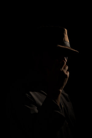 Discreet portrait of detective man with hat in darkness. Dark room art.の写真素材