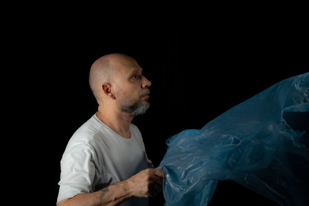 Man holding a blue plastic bag against black background.の写真素材