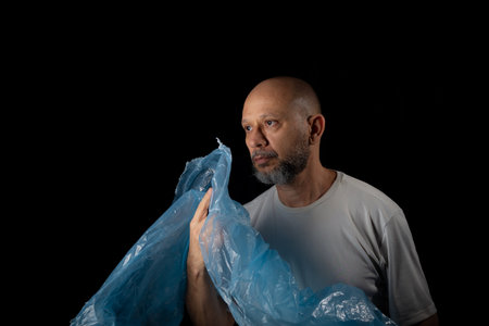 Man holding a blue plastic bag against black background.の写真素材