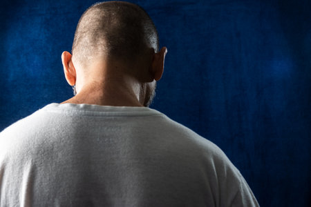 Man, with his back turned, sad, head down against blue background.の写真素材