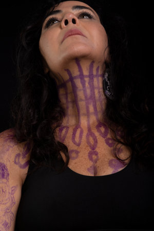 Beautiful woman with tattooed and painted body looking up against black background.の写真素材
