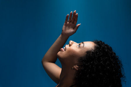 Close-up portrait of beautiful young woman, with curly hair, with her hand raised and looking up....