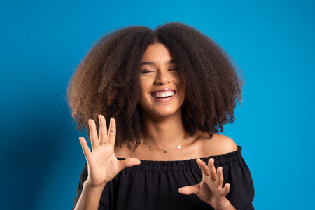 Beautiful young woman with black power hair smiling and looking at the camera. Isolated on blue...