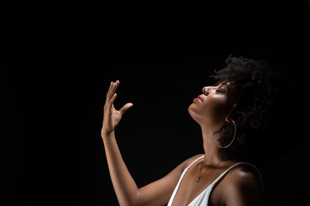 Beautiful woman, with black power hair, making movements with her arms. Wearing white clothes. Isolated on black background.の写真素材