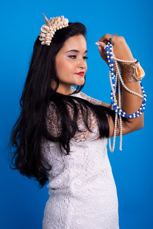 Beautiful, black-haired woman with shell tiara on her head holding and looking at pearl necklaces....