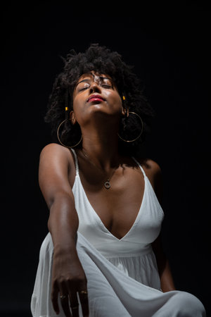 Beautiful woman, with black hair, sitting wearing white clothes and posing for the camera. isolated on black background.の写真素材