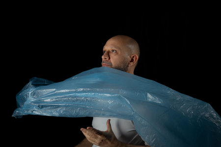 Man holding a blue plastic bag against black background.の写真素材