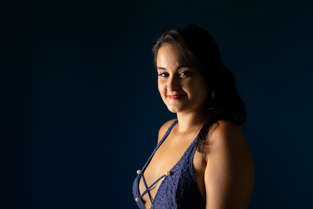 Portrait in a blue dress against a dark blue background, showing confidence and elegance in studio lighting.の写真素材