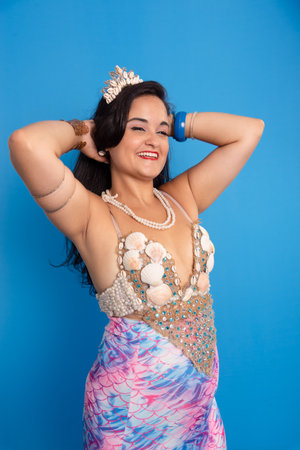 Beautiful woman, wearing a tiara and seashell bracelets, against a blue background, touching her black hair. Yemanja worshiper.の写真素材
