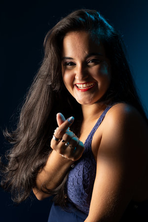 Portrait of a person with black hair, cheerful, confident, in a blue dress, looking at the camera. Isolated on dark blue background.の写真素材