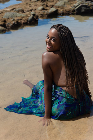 Half-closed portrait of a beautiful woman, with braids, with her back looking at the camera. sunbathing on the beach. Against blue sky.の写真素材