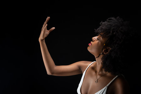Beautiful woman, with black power hair, making movements with her arms. Wearing white clothes. Isolated on black background.の写真素材