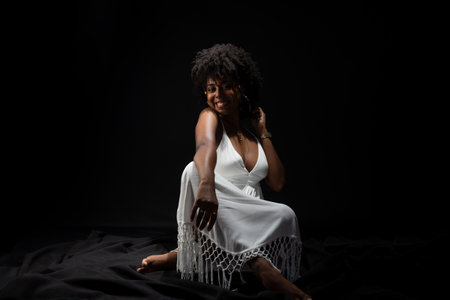 Beautiful woman, with black hair, sitting wearing white clothes and posing for the camera. isolated on black background.の写真素材