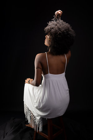 Beautiful woman, with black hair, sitting wearing white clothes and posing for the camera. isolated on black background.の写真素材