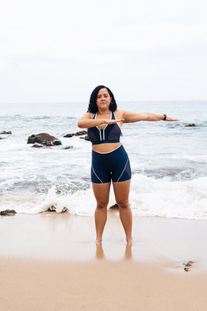 Fitness woman, standing, doing exercises with her arms on the beach sand against the sea and cloudy sky. Healthy lifestyle.の写真素材