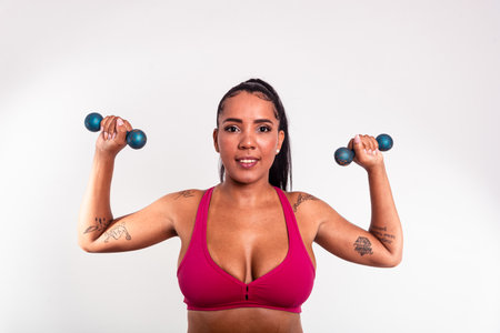 Beautiful woman dressed in gym clothes holding dumbbells above her shoulder. Healthy life with physical exercise.の写真素材