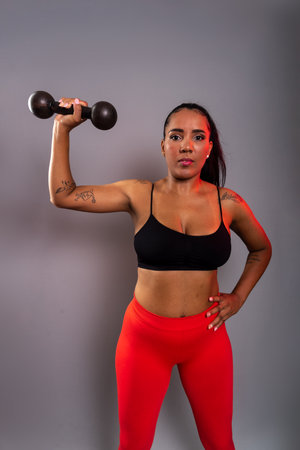 Beautiful brunette woman, in gym clothes, holding black dumbbells at head height. Healthy life. Against gray background.の写真素材