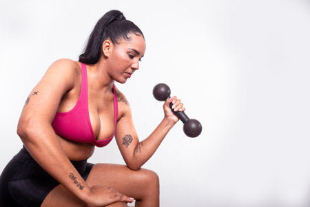 Young fitness woman, dressed in gym clothes, sitting doing arm exercises with dumbbells. Healthy life with physical exercise.の写真素材