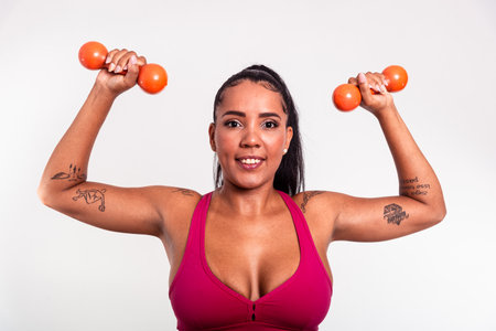 Beautiful woman dressed in gym clothes holding dumbbells above her shoulder. Healthy life with physical exercise.の写真素材