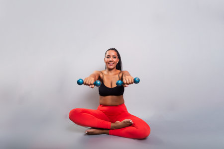 Beautiful, brunette, happy and smiling woman in gym clothes, sitting holding dumbbells. Healthy life. Against gray background.の写真素材