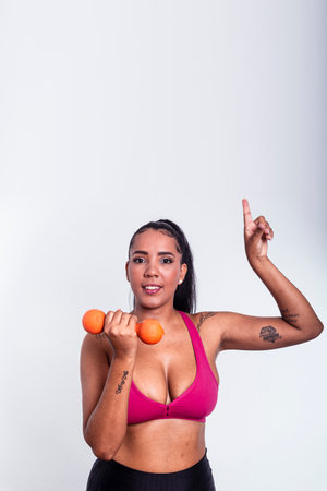 Beautiful woman dressed in gym clothes holding dumbbells and pointing fingers up. Healthy life with physical exercise.の写真素材