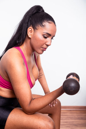 Young fitness woman, dressed in gym clothes, sitting doing arm exercises with dumbbells. Healthy life with physical exercise.の写真素材