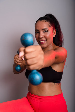 Beautiful, brunette, happy and smiling woman in gym clothes, holding dumbbells and looking at the camera. Healthy life. Against gray background.の写真素材