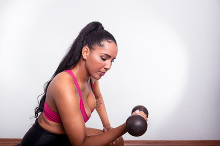 Young fitness woman, dressed in gym clothes, sitting doing arm exercises with dumbbells. Healthy life with physical exercise.の写真素材