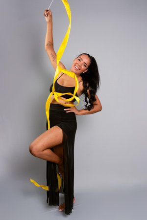 Beautiful gymnast woman doing acrobatic moves with a yellow ribbon. Isolated on gray background.の写真素材