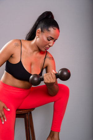 Beautiful brunette woman, in gym clothes, sitting doing exercises with dumbbells. Healthy life. Against gray background.の写真素材