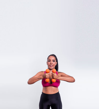 Young fitness athlete woman, dressed in gym clothes, holding dumbbells at torso height. Healthy life with physical exercise.の写真素材