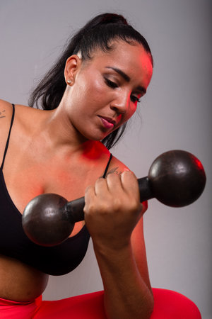 Beautiful brunette woman, in gym clothes, sitting doing exercises with dumbbells. Healthy life. Against gray background.の写真素材