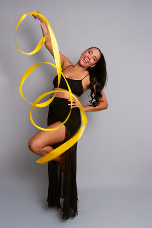 Beautiful gymnast woman doing acrobatic moves with a yellow ribbon. Isolated on gray background.の写真素材