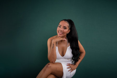 Beautiful young adult brunette woman sitting wearing white clothes posing for photo. Isolated on green background.の写真素材