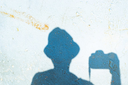 Shadow of an unidentified person on the wall wearing a hat and holding a professional photography camera. Texture.の写真素材