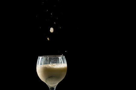 Drops of milk falling into a wine glass. Isolated on black background.の写真素材