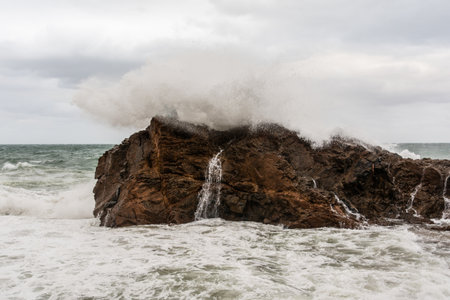 Immense waves hitting a large rock at the edge of the beach. Force of nature. Winterの写真素材