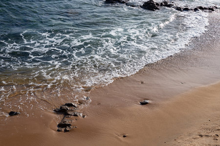 Seaside of a beach with small foaming waves. Sunny day, calm sea water.の写真素材
